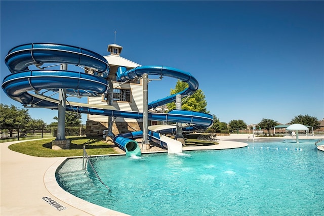 community pool with a water play area, fence, and a water slide