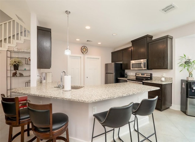 kitchen featuring a peninsula, visible vents, a kitchen bar, appliances with stainless steel finishes, and a sink