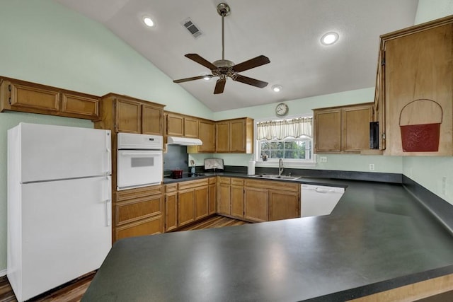 kitchen featuring white appliances, dark countertops, under cabinet range hood, visible vents, and a sink
