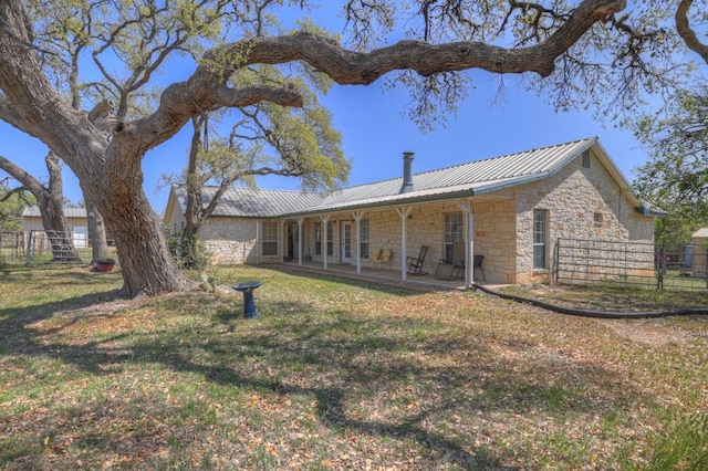 rear view of property featuring a yard, metal roof, fence, and stone siding
