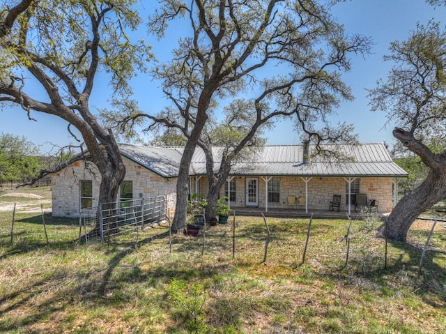 rear view of house with metal roof, fence, stone siding, and a lawn
