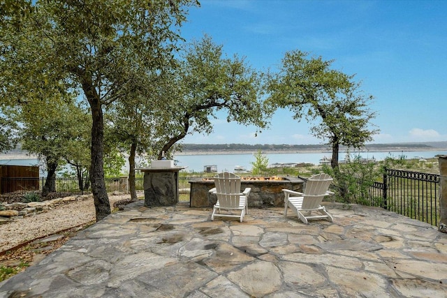 view of patio featuring fence, a water view, and an outdoor fire pit