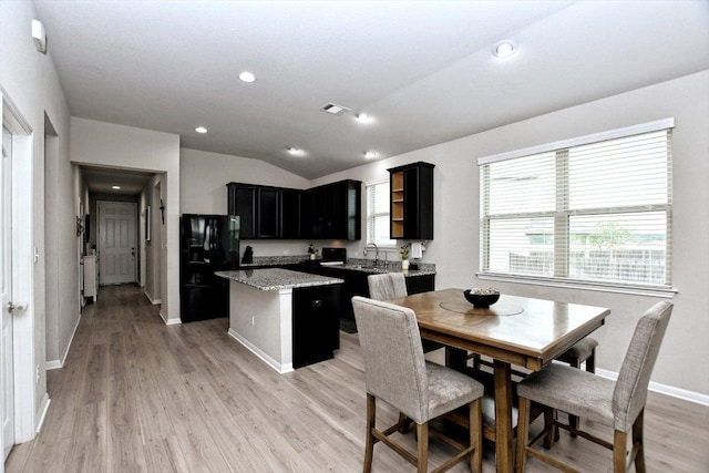 5741 Porano Cir, Round Rock, TX 78665 - kitchen with black fridge, a kitchen island, dark cabinets, lofted ceiling, and light wood-style flooring