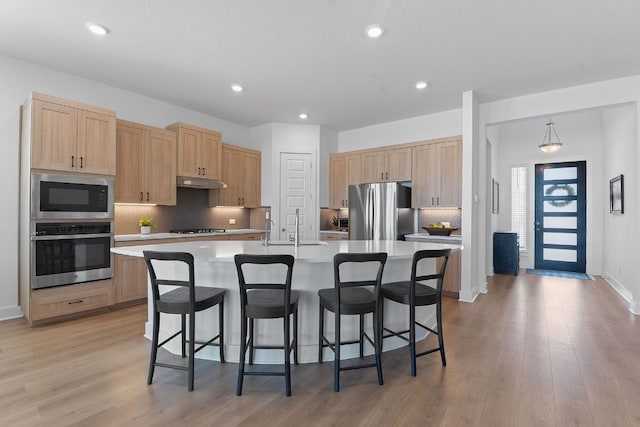 kitchen featuring light brown cabinetry, a sink, a kitchen bar, and appliances with stainless steel finishes