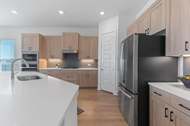 kitchen with under cabinet range hood, light brown cabinetry, stainless steel appliances, and a sink