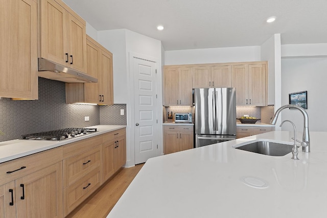 kitchen with appliances with stainless steel finishes, light brown cabinets, under cabinet range hood, and a sink
