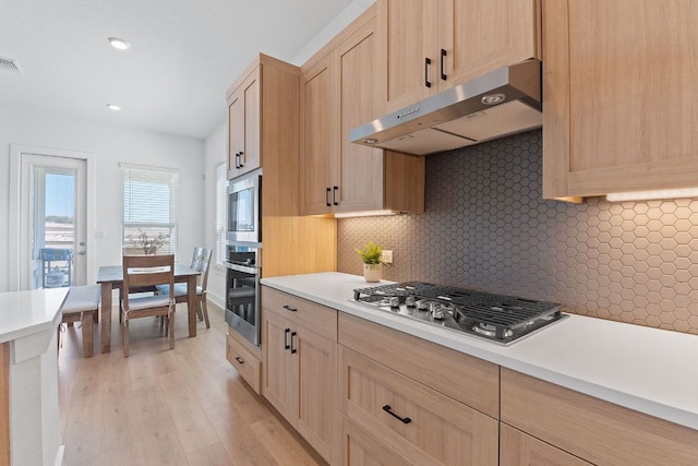 kitchen with under cabinet range hood, stainless steel appliances, light brown cabinetry, and light countertops