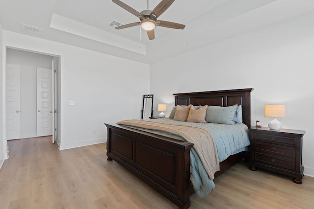 bedroom with light wood finished floors, baseboards, visible vents, and a raised ceiling