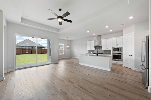 kitchen with visible vents, wall chimney exhaust hood, open floor plan, a ceiling fan, and appliances with stainless steel finishes