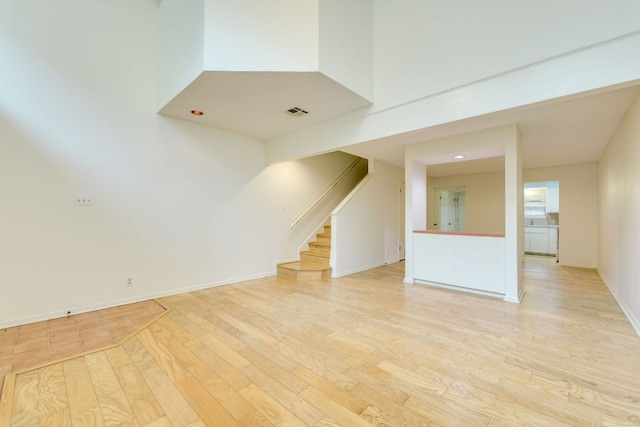 unfurnished living room featuring stairway, visible vents, light wood finished floors, and baseboards