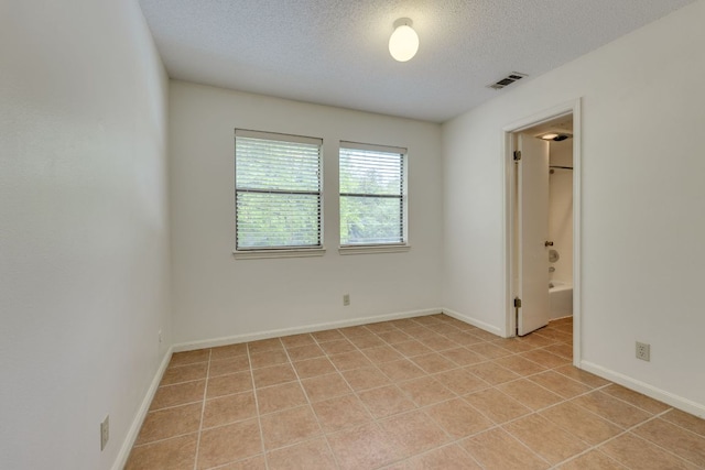 unfurnished room with a textured ceiling, visible vents, baseboards, and light tile patterned flooring