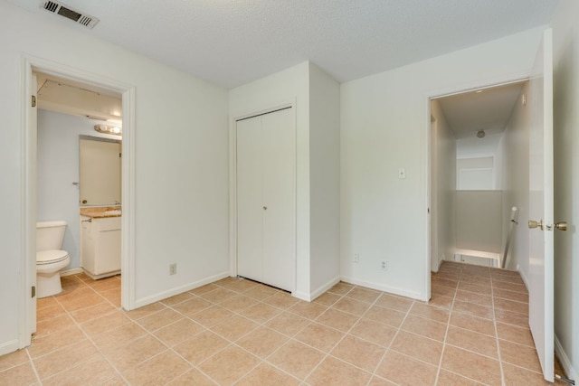 unfurnished bedroom featuring light tile patterned floors, visible vents, ensuite bathroom, baseboards, and a closet