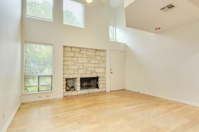 unfurnished living room featuring baseboards, visible vents, wood finished floors, and a high ceiling