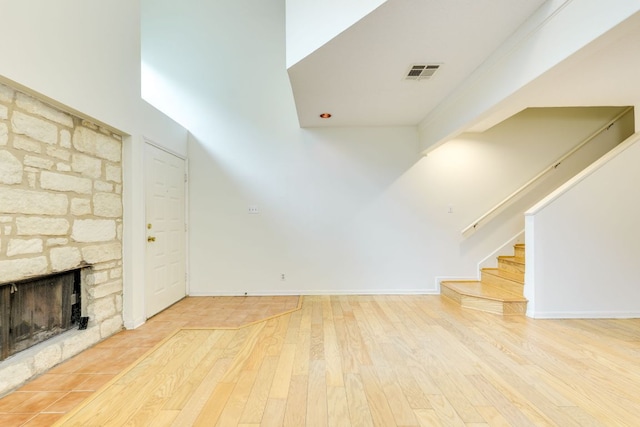 unfurnished living room with stairway, wood finished floors, a stone fireplace, visible vents, and lofted ceiling
