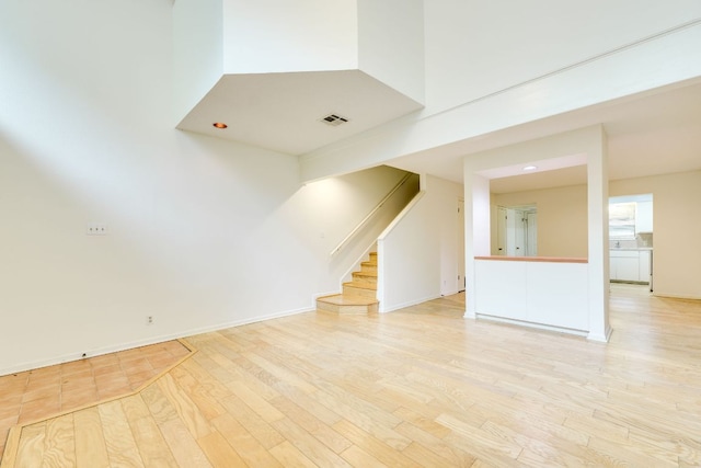 unfurnished living room featuring visible vents, stairway, light wood-style floors, and baseboards