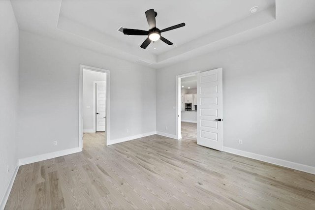 unfurnished room featuring a ceiling fan, baseboards, light wood-style flooring, and a raised ceiling