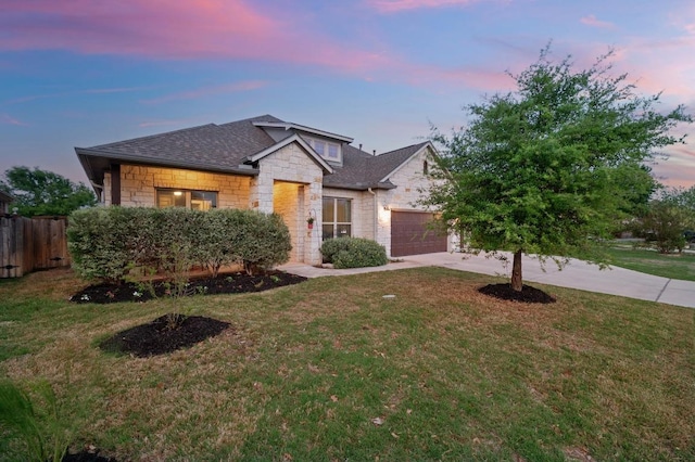 view of front of home with roof with shingles, a front yard, fence, stone siding, and driveway