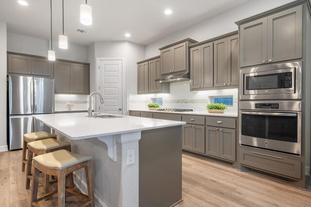 kitchen with a sink, light wood-type flooring, under cabinet range hood, stainless steel appliances, and gray cabinets