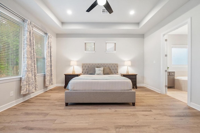 bedroom featuring a tray ceiling, light wood-style floors, baseboards, and visible vents