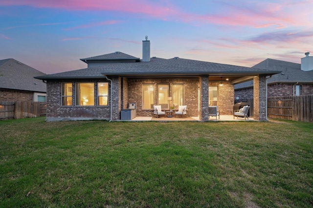 back of house at dusk with a patio, a yard, and a fenced backyard