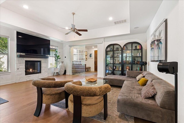 living area with a fireplace, a raised ceiling, a ceiling fan, visible vents, and wood finished floors