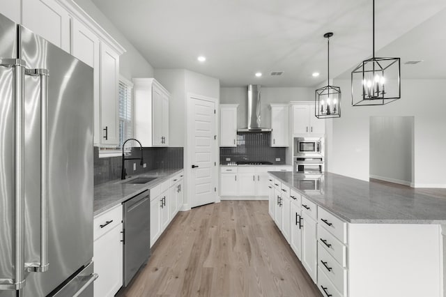 kitchen with a sink, wall chimney range hood, recessed lighting, a center island, and appliances with stainless steel finishes