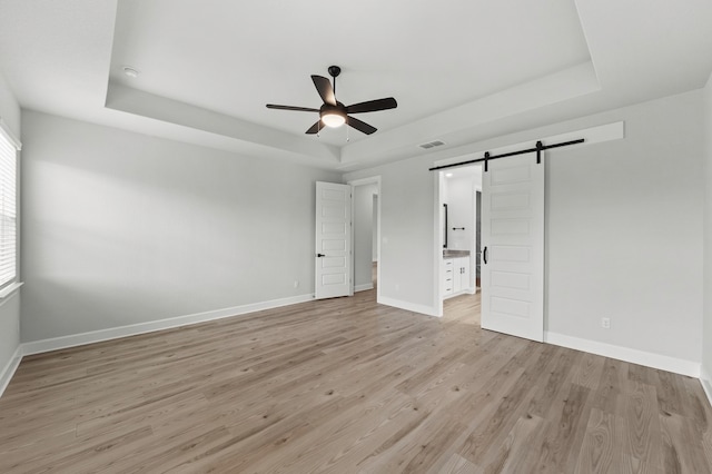 unfurnished bedroom featuring baseboards, a tray ceiling, a barn door, and light wood-style flooring