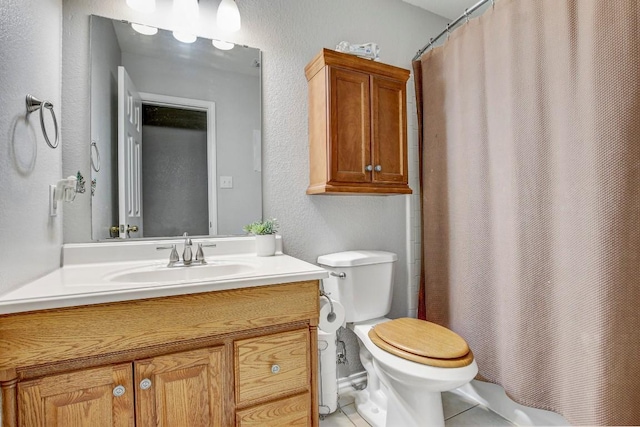 bathroom featuring tile patterned floors, vanity, a textured wall, and toilet