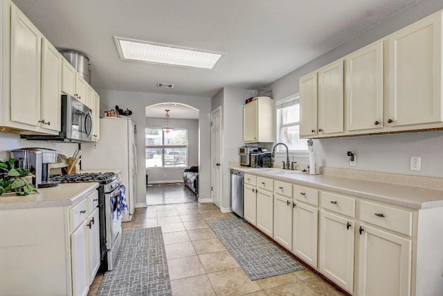 kitchen featuring a sink, arched walkways, appliances with stainless steel finishes, light countertops, and light tile patterned floors