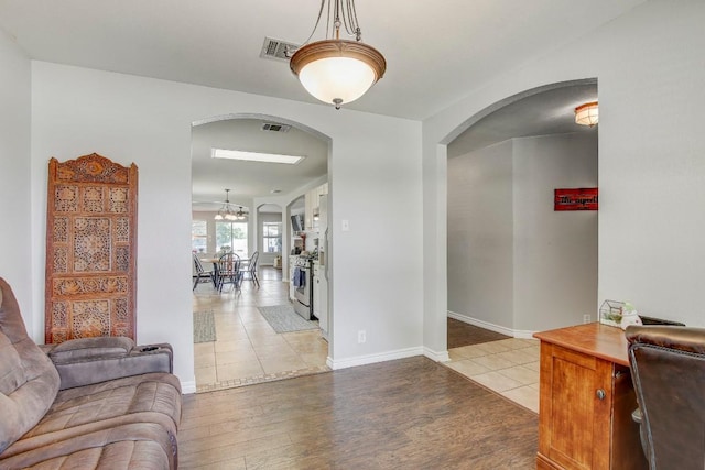 interior space featuring light wood-type flooring, baseboards, visible vents, and arched walkways