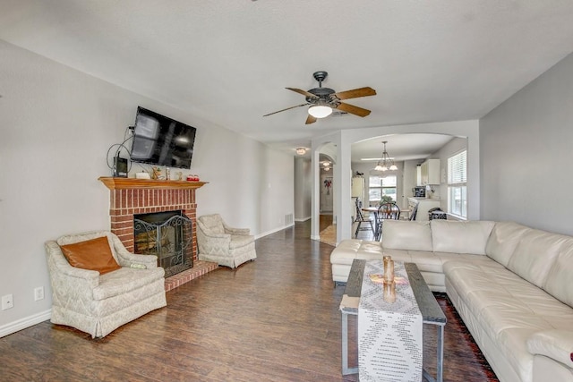 living area featuring wood finished floors, arched walkways, baseboards, a fireplace, and ceiling fan with notable chandelier