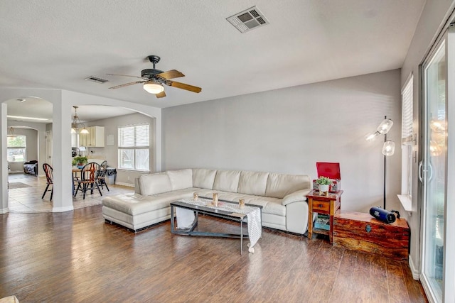 living room featuring arched walkways, plenty of natural light, visible vents, and ceiling fan