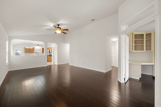 unfurnished living room featuring baseboards, arched walkways, dark wood-style flooring, a ceiling fan, and vaulted ceiling