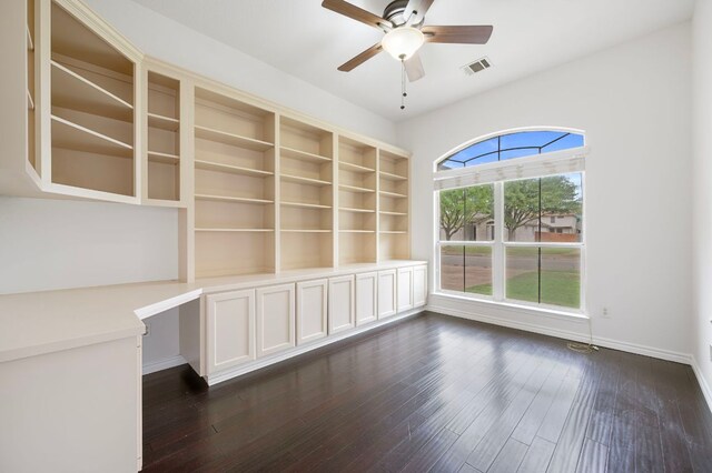 interior space with a ceiling fan, built in desk, dark wood finished floors, and visible vents