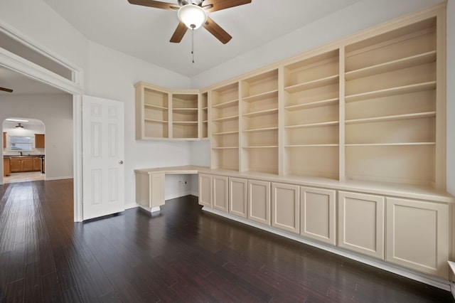 unfurnished office with dark wood-style flooring, baseboards, a ceiling fan, and arched walkways