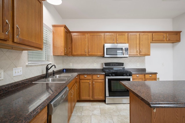 kitchen with brown cabinetry, appliances with stainless steel finishes, a sink, and backsplash