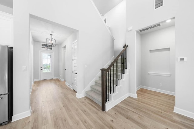 foyer with light wood finished floors, a notable chandelier, visible vents, baseboards, and stairs
