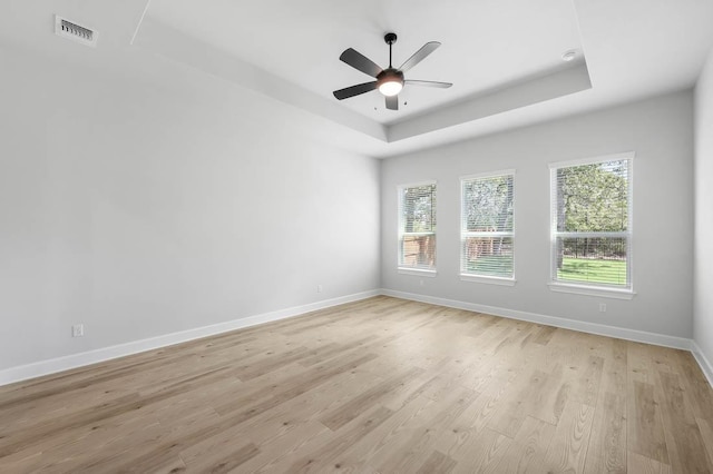 empty room with visible vents, light wood finished floors, ceiling fan, a raised ceiling, and baseboards