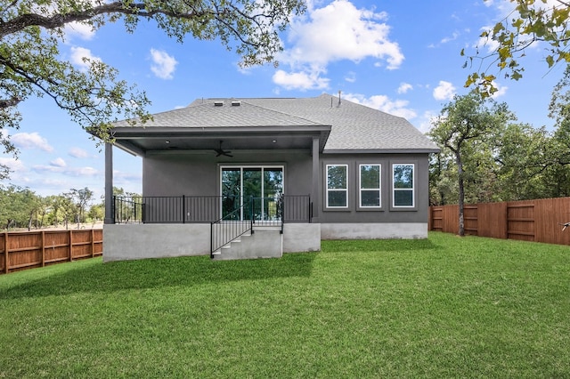 rear view of property featuring a ceiling fan, stucco siding, roof with shingles, and a lawn