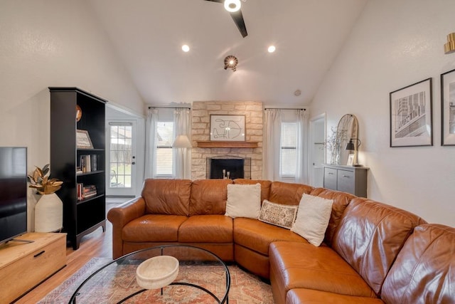 living area featuring light wood-type flooring, a healthy amount of sunlight, ceiling fan, and a stone fireplace