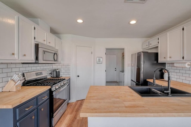 kitchen with blue cabinetry, white cabinets, appliances with stainless steel finishes, a sink, and wooden counters