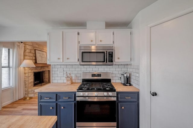 kitchen with tasteful backsplash, blue cabinetry, white cabinets, stainless steel appliances, and wooden counters