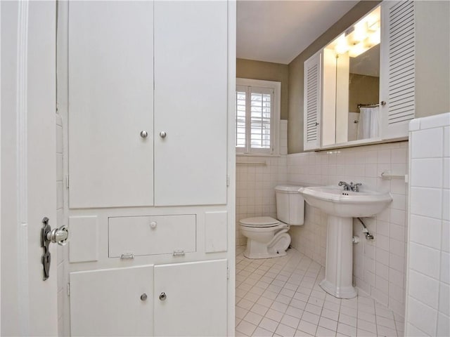 full bathroom with toilet, tile patterned floors, tile walls, and a sink