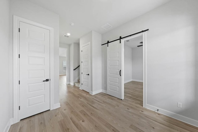 empty room featuring baseboards, visible vents, light wood-style flooring, and a barn door