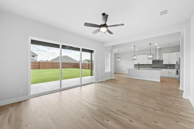 unfurnished living room featuring baseboards, light wood finished floors, ceiling fan, visible vents, and a sink
