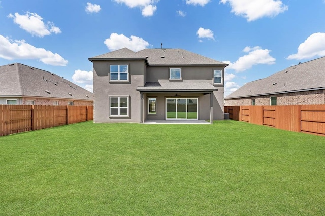 rear view of property with a ceiling fan, stucco siding, a fenced backyard, and a lawn