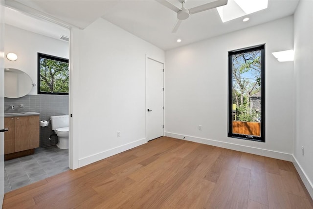 2218 Haskell St, Austin, TX 78702 - unfurnished bedroom featuring a skylight, light wood-style floors, connected bathroom, recessed lighting, and ceiling fan