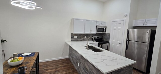 kitchen with a high ceiling, appliances with stainless steel finishes, a sink, dark wood finished floors, and a peninsula