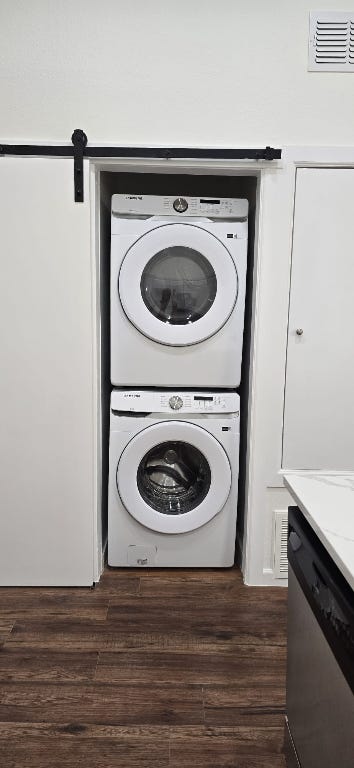 laundry area featuring visible vents, laundry area, stacked washing maching and dryer, and dark wood-type flooring