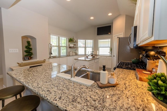 702 Silo St, San Marcos, TX 78666 - kitchen featuring white cabinets, stainless steel microwave, light stone counters, lofted ceiling, and a kitchen bar